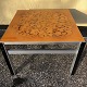 Square coffee 
table with 
glass top, 
metal frame and 
black painted 
wood in the 
corners. Traces 
of ...