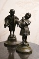 2 små 
dekorative 
bronze figurer 
af dreng med 2 
grise under 
armen og pige 
der holder en 
gås. H: ...