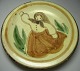 Plate in 
ceramics, 
decorated with 
a woman in 
a long dress 
and scarf, 
light slip with 
green and ...