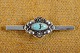 Brooch 
elongated 
decorated with 
cabochon cut 
turquoise 
mounted with 
silver flowers 
and leaves. ...
