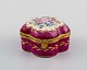 Antique lidded 
box in 
hand-painted 
porcelain with 
flowers and 
gold decoration 
on a purple ...