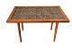 Small table in teak veneer with slightly inclined legs in solid teak wood. Tiles in a brownish ...