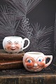 Old faience cups with handles and funny faces from around 1930.Measurements: H: 6.5cm. Dia.: ...